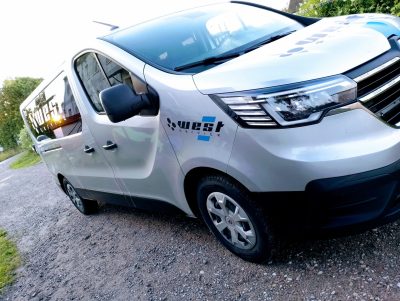 Srebrny van Renault West Service zaparkowany na żwirowej drodze przy zieleni