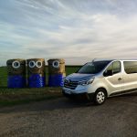 Srebrny bus na tle zachodzącego słońca. obok busa ustawione są snopki siana, przypominające postaci z filmu animownego 